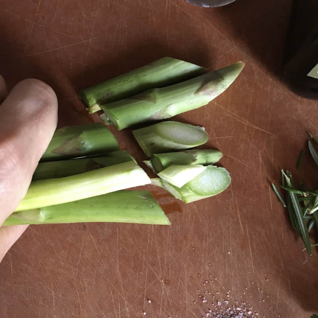 sliced asparagus ends on the cutting board next to my hand which is holding the asparagus spears in a bundle