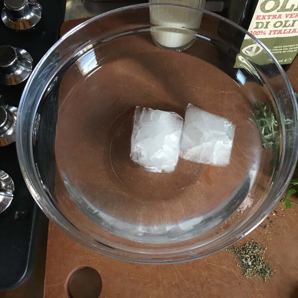 bowl of water in a clear mixing bowl with two large king sized ice cubes floating in it all on top of a cutting board