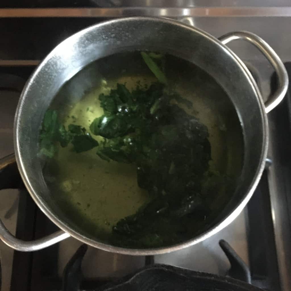 blanching asparagus and spinach leaves in a small stainless steel pot of salted water