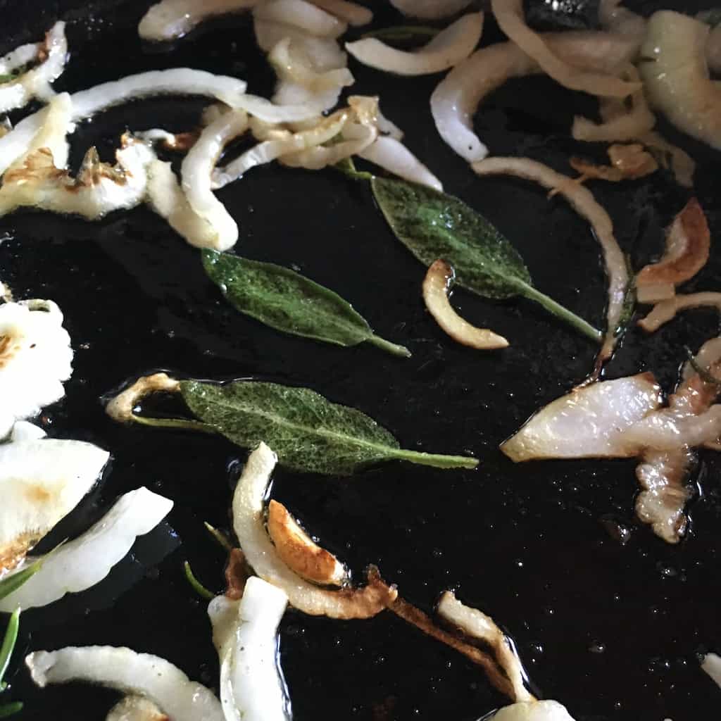 3 sage leaves in the middle of caramelizing onions in cast-iron skillet