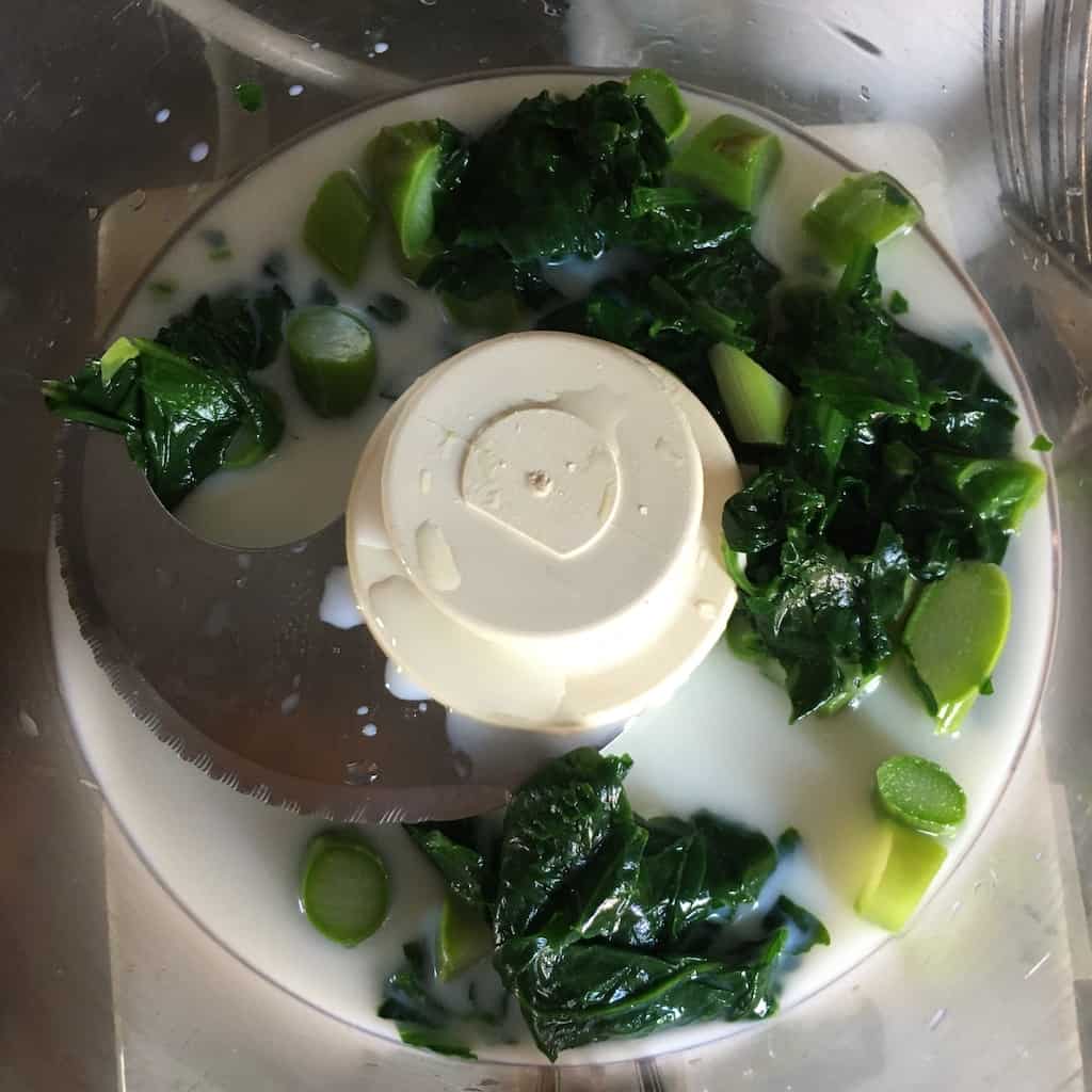 blanched asparagus ends and spinach with milk in bowl of food processor