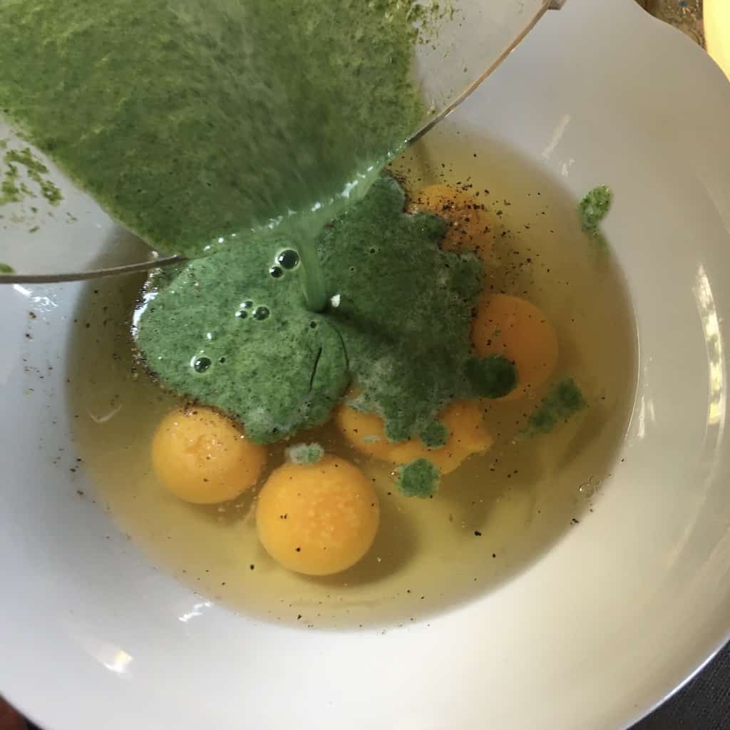 pouring the green mixture into the 6 eggs cracked into a white bowl with salt and freshly cracked black pepper