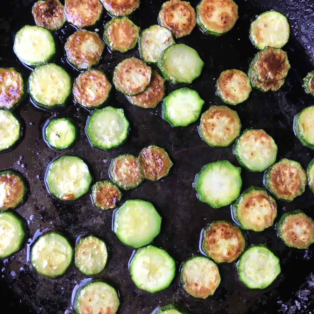 beautifully browning zucchini rounds cooking after being flipped over to reveal the golden cooked color