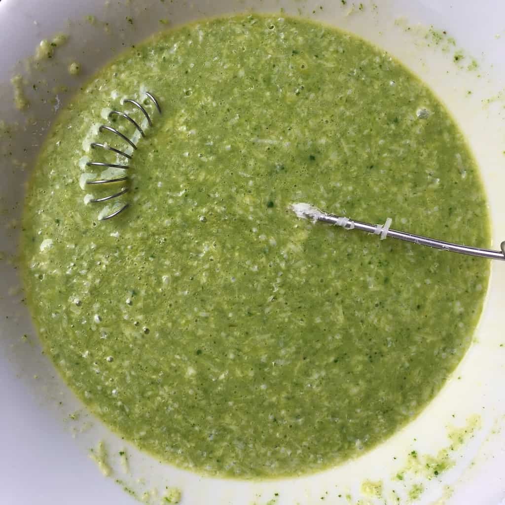 closeup of spring green mixture and specks of grated cheese in a white bowl with whisk