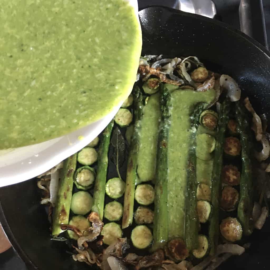 pouring the green egg mixture over the nicely laid out vegetables in the cast iron skillet