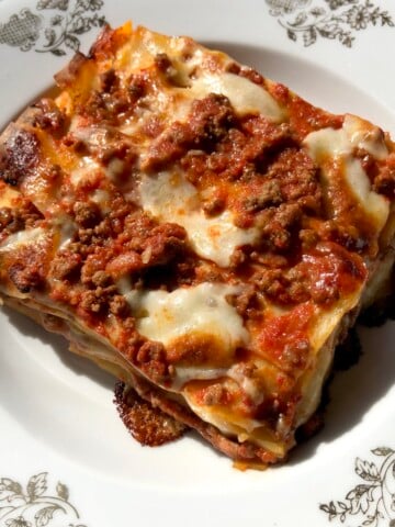 A portioned square of "almost lasagna bolognese" pasta bake with beef ragu, porcini bechamel, mozzarella cheese, and parmigiano-reggiano cheese.
