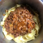 A pot with bolognese sauce added to buttery pappardelle noodles before being tossed
