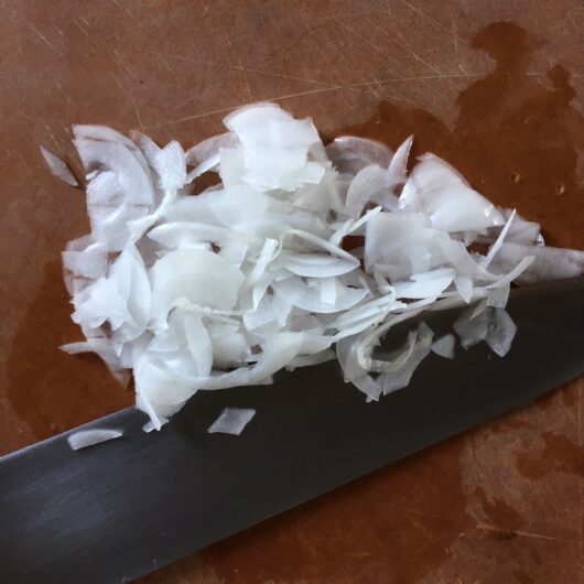sliced and chopped onions lying on a cutting board with the chef knife next to it