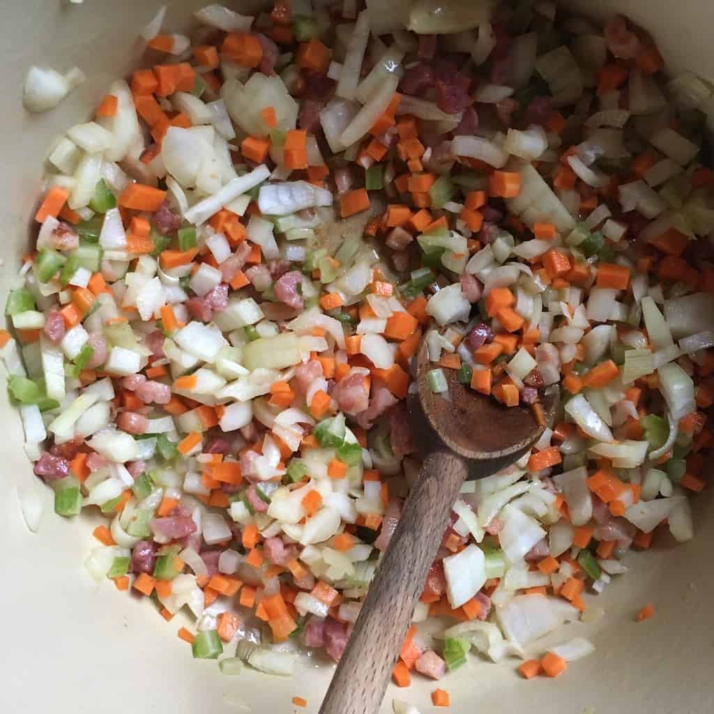 mirepoix of veggies mixed together with the pancetta and olive oil with a wooden spoon in the pot
