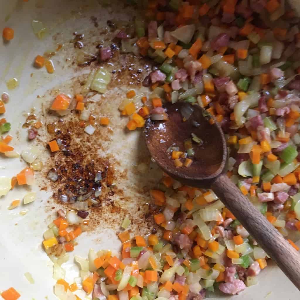 the veggies and pancetta mix has noticeably lost much of it's moisture as the veggies cook and flavors are being concentrated plus, you can see lots of the fond at the bottom of the pan even more now than earlier and the wooden spoon is there stirring the veggies around