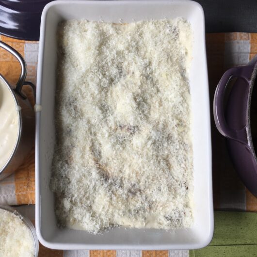 bechamel covered lasagna dish with grated parmigiano cheese sprinkled evenly over the top