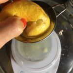 squeezing a fresh lemon into a measuring cup with a small strainer catching the seeds