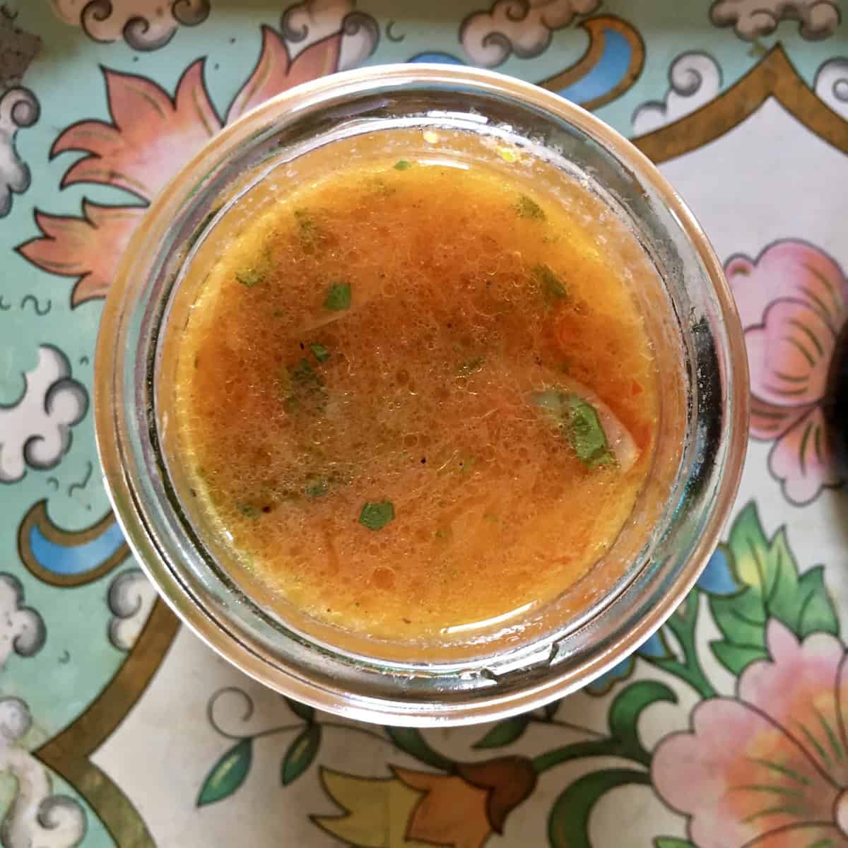 Homemade Lemon-tomato vinaigrette with herbs in a glass Weck canning jar on top of a decorative vintage tray with pink, white and green flowers.