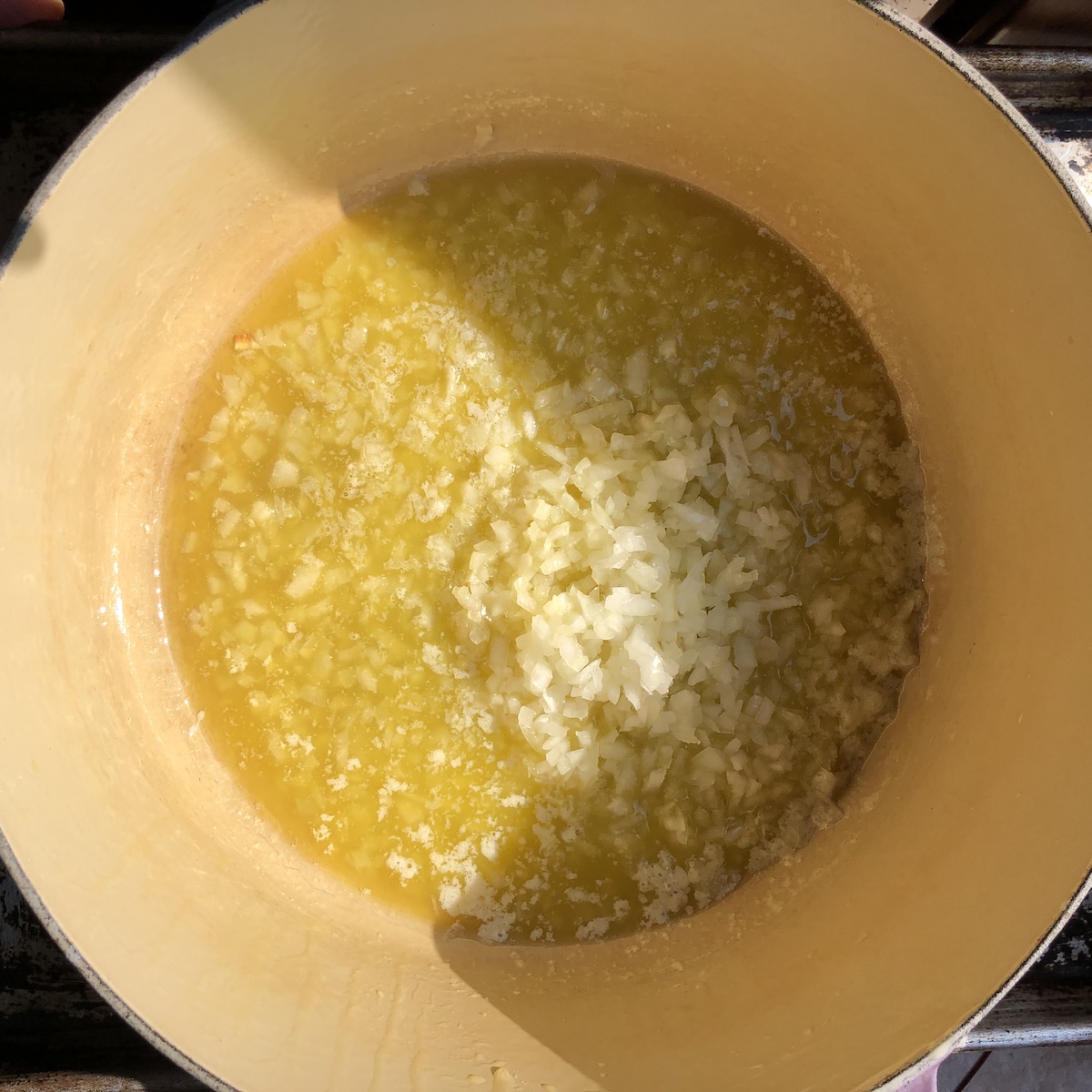 Adding finely diced onions to a Dutch oven with olive oil and melted butter to start the soffrito for a bolognese sauce, showing  how to make bolognese sauce by sauteeing each vegetable individually to concentrate flavor.

