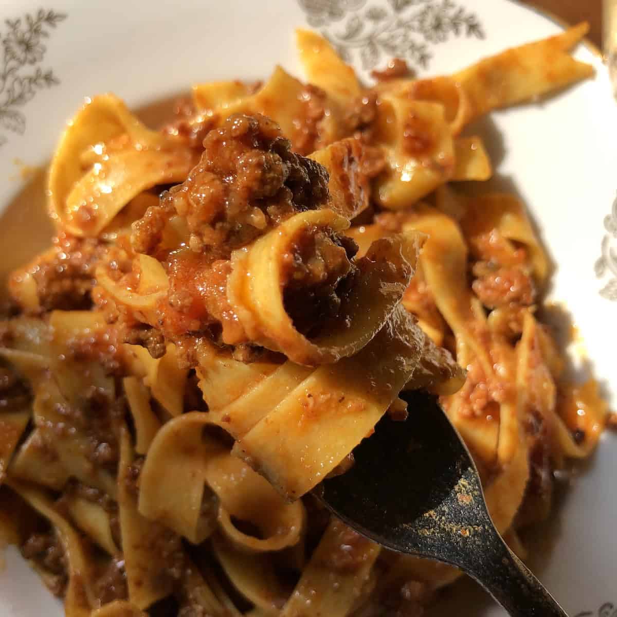 Pasta bolognese with homemade pappardelle twirled on a fork ready to eat, authentic bolognese sauce recipe with a traditional bolognese ragu on fresh pasta.
