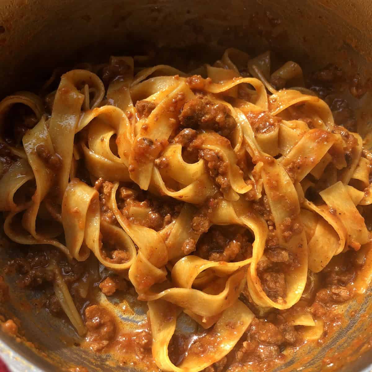 Pasta bolognese with silky pappardelle mixed together in a pot ready to be plated, pasta bolognese recipe tossed with a rich ragu bolognese for a simple bolognese recipe.