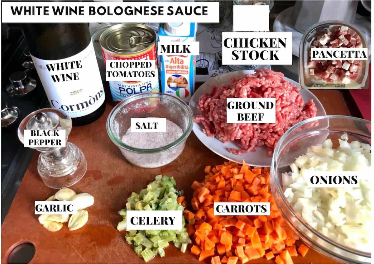 Labeled white bolognese sauce ingredients on a cutting board with white wine for a best bolognese recipe variation, traditional bolognese sauce made with white wine instead of red.