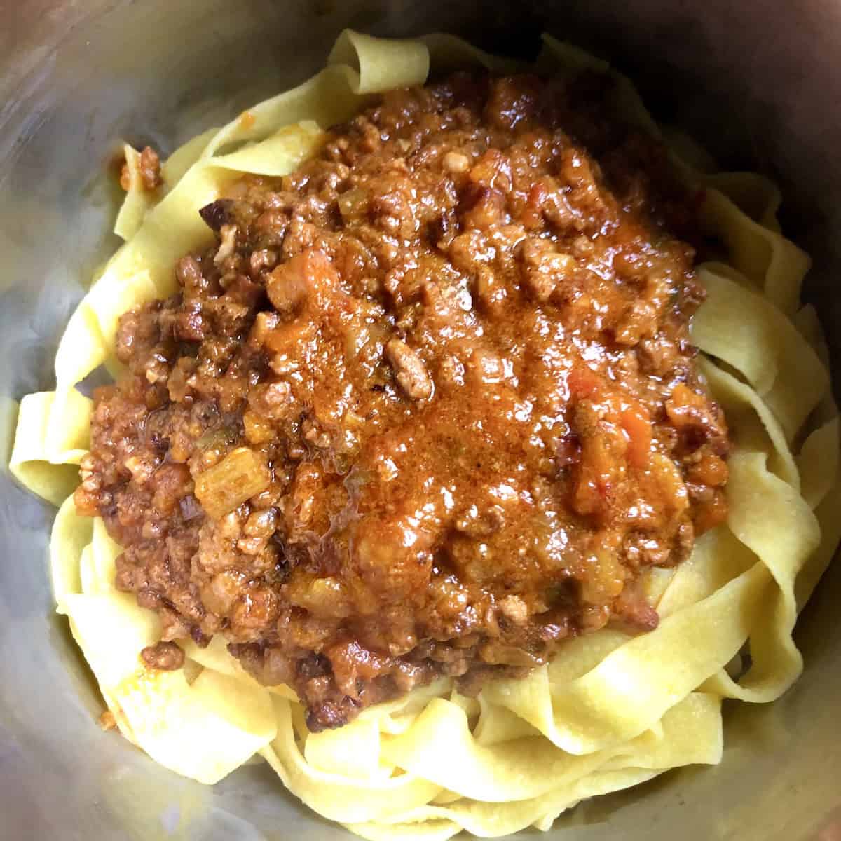 White wine bolognese sauce added to pappardelle pasta in a pot ready to be mixed, pasta bolognese recipe variation with a lighter Italian ragu made with white wine.
