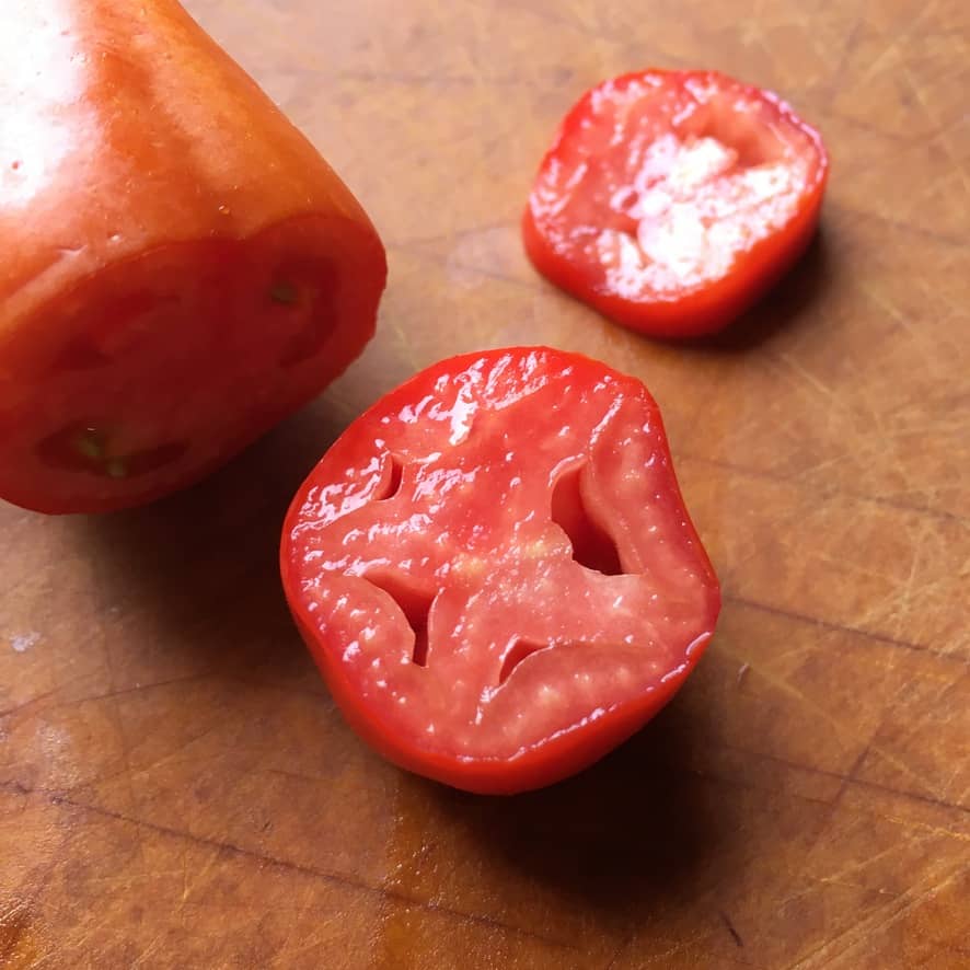 san marzano cornabel tomato sliced into rounds revealing the fleshy interior that appears to be almost seedless resting on a cutting board