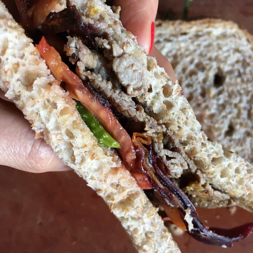 my hand holding up one half of the sandwich on whole wheat sandwich bread showing the slices of beef, tomato, cucumbers and carrot ribbons inside