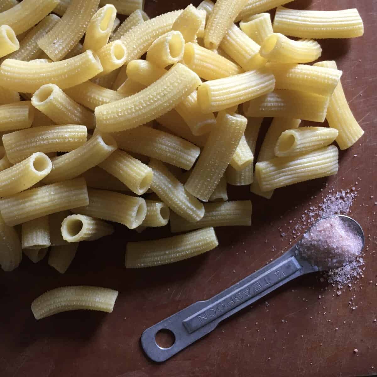 maccheroni fresh egg pasta uncooked lying on a cutting board with a vintage aluminum teaspoon holding pink Himalayan salt s