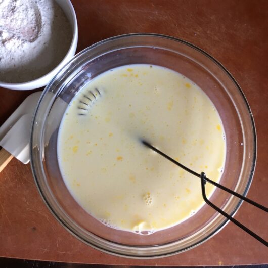 a mixing bowl with eggs and milk whisked together looking pale yellow