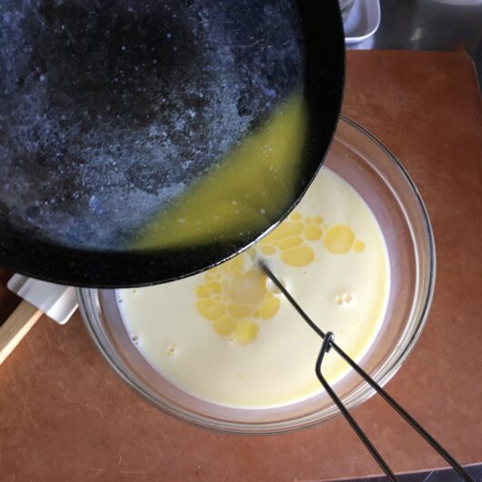 golden melted butter being added to the whisked milk mixture