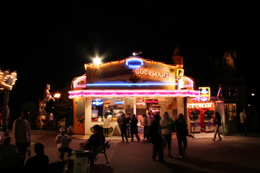 a food stand near the Eiffel Tower in Paris, France with pink, blue and yellow neon lights and crowds of people enjoying l