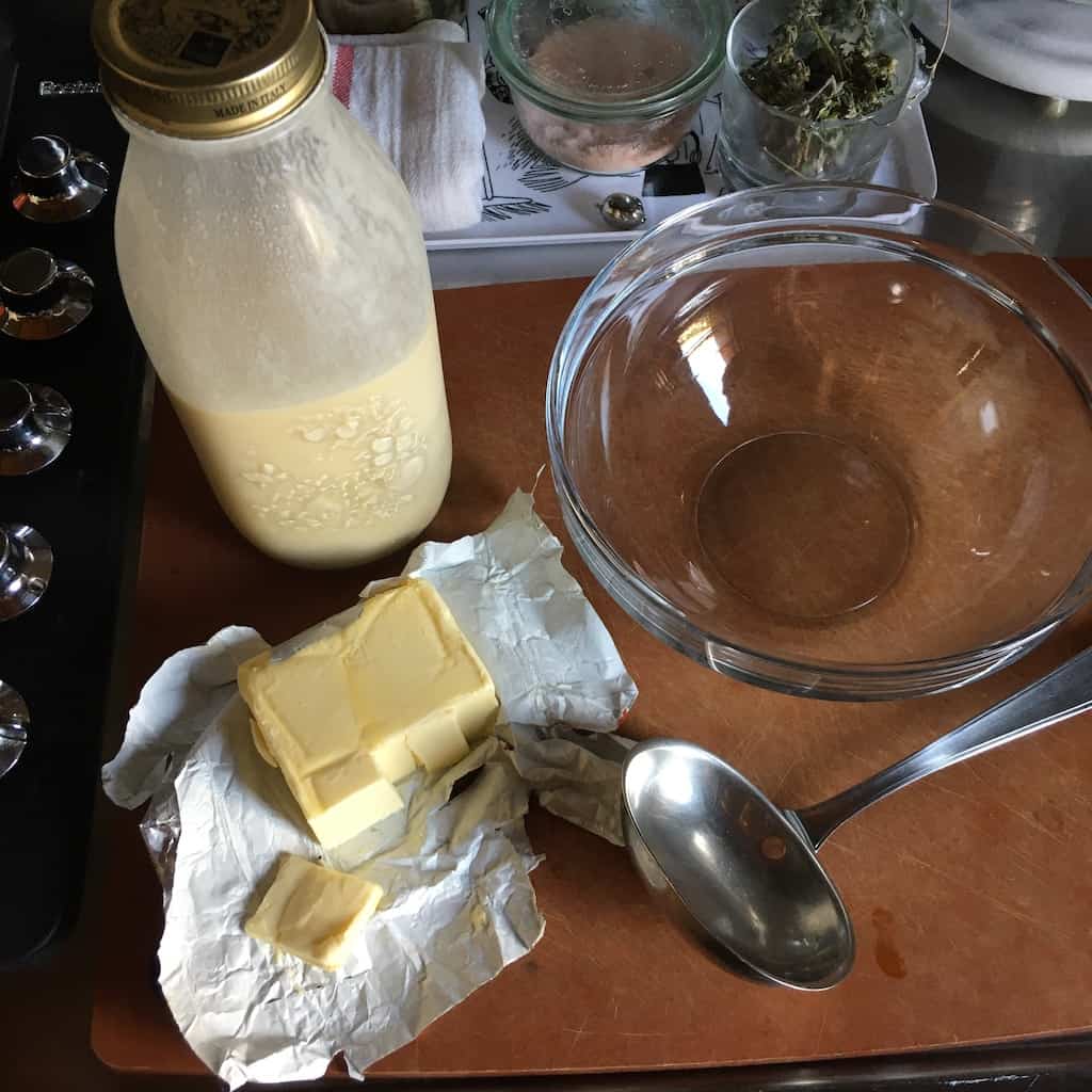 crêpe batter in a tall jar next to an open package of butter, an empty clear glass mixing bowl and ladle