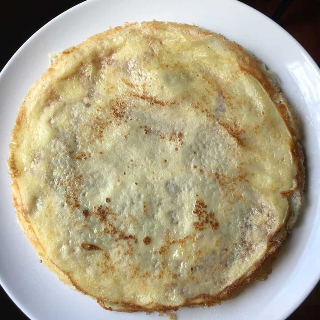 a large white platter with a stack of beautifully golden crêpes with sporadic brown spots