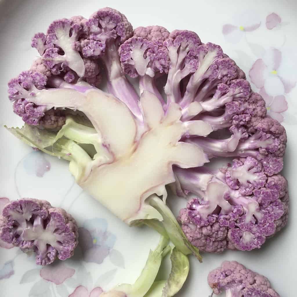 purple cauliflower steak on white ceramic platter with similar colored flowers pattern