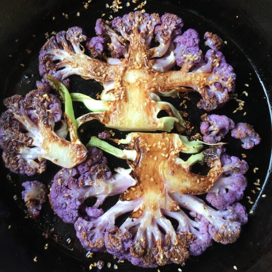 perfectly golden brown purple cauliflower steaks covered with toasty sesame seeds