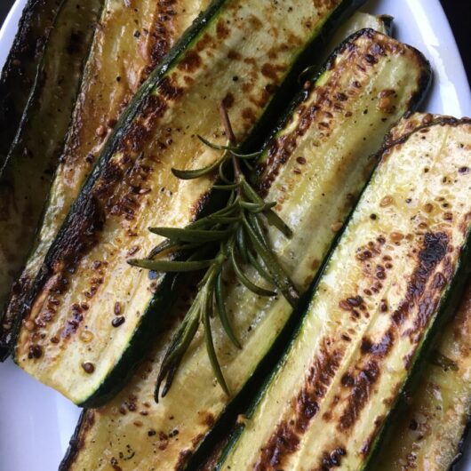 pan-seared caramelized and golden brown zucchini slices on a white platter and a sprig of crispy rosemary on top