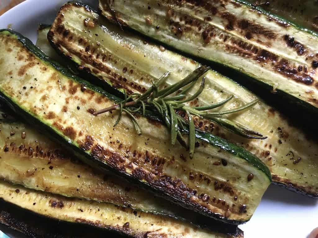 pan-seared caramelized and golden brown zucchini slices on a white platter and a sprig of crispy rosemary on top