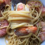 a large orange and pink shrimp with spaghetti all twirled around a fork looking super tasty and ready to be eaten