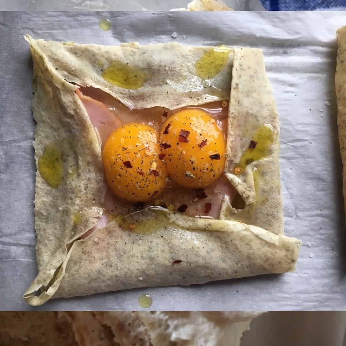 A folded crepe framing two cracked eggs with ham, salt, and pepper ready to bake, a savory crepe recipe for breakfast crepes with eggs or brunch.
