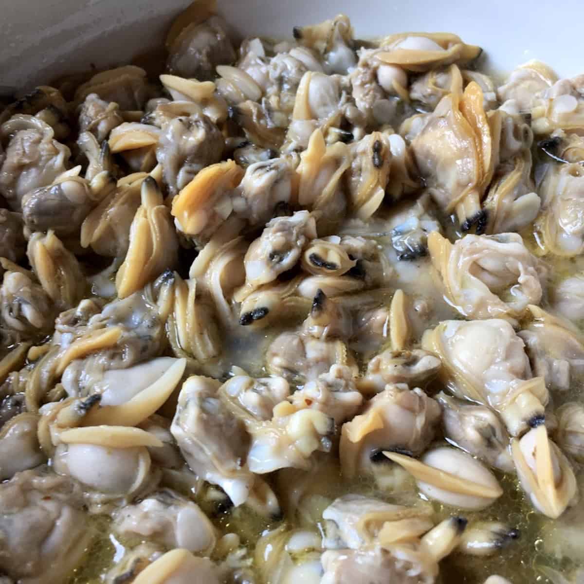 Bowl of shelled fresh clams in clam liquor ready to be strained free of sand and grit and added to linguine alle vongole sauce, vongole bianco preparation.