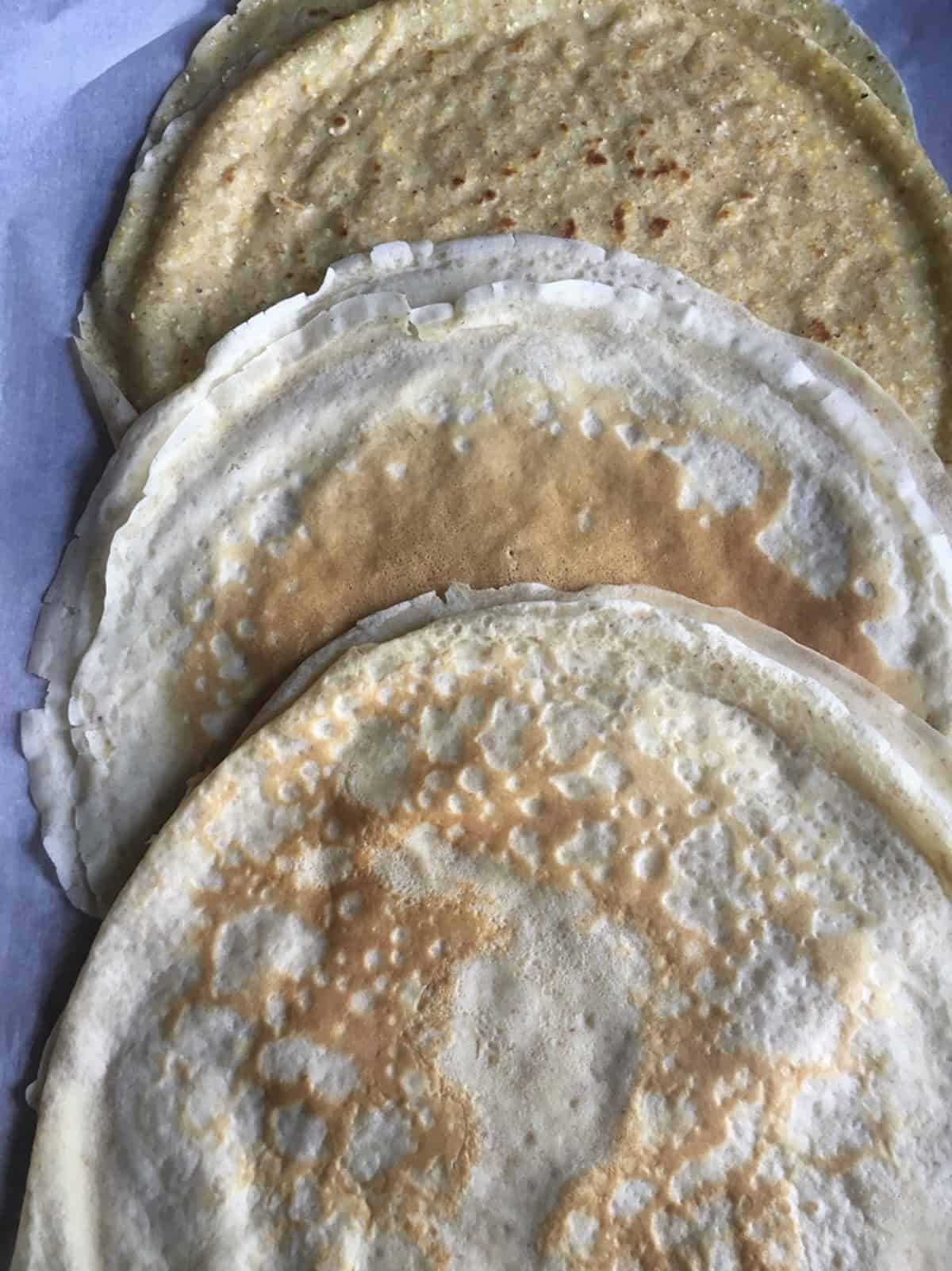 Three stacks of crepes showing different crepe ingredients addins and types including cornmeal crepes, oatmeal crepes, and classic french crepes for a simple crepe recipe with texture variations.