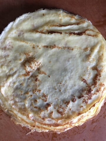 Stack of homemade French crepes with golden brown toasted spots, thin and delicate classic crepes ready to fill.