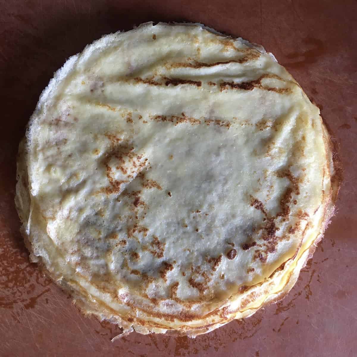 Stack of homemade French crepes with golden brown toasted spots, thin and delicate classic crepes ready to fill.