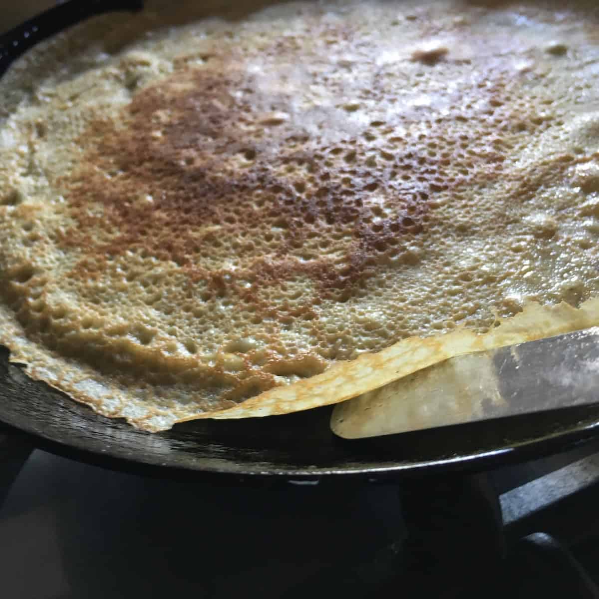 Using an offset spatula to flip a crepe in the pan, showing how to flip a crepe easily for perfect crepes every time in this simple crepes recipe.