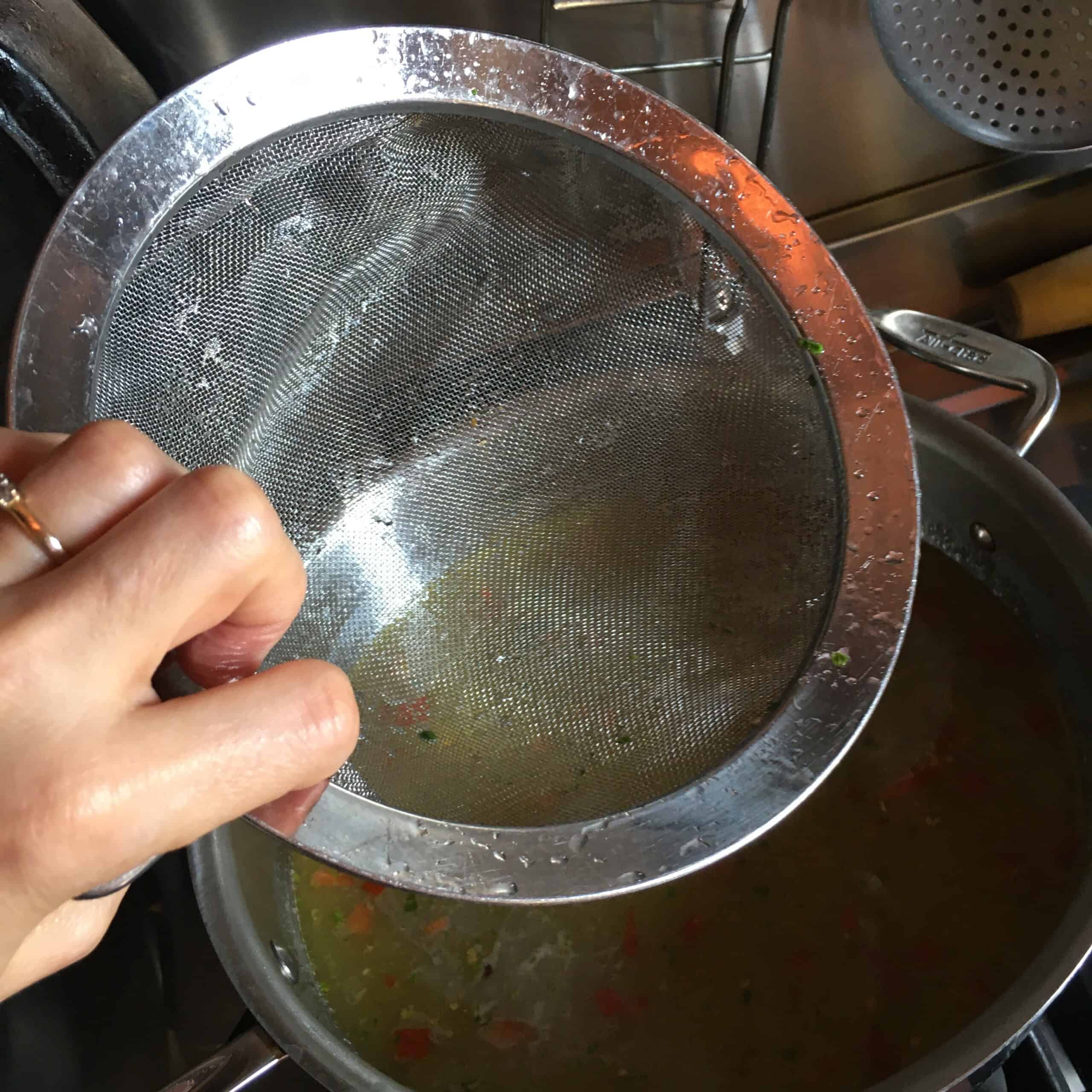 Straining clams and clam liquor through a fine mesh strainer to remove sand and grit for linguine with clam sauce recipe.