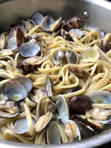 A saute pan of homemade linguine with clam sauce in a white wine clam sauce with shells on, linguine and clams recipe tossed made with Italian Veraci clams and linguine pasta.