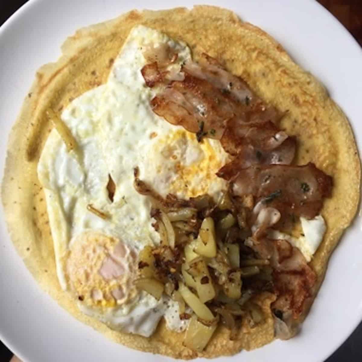 Open faced crepe topped with eggs, ham, and caramelized onions, a savory breakfast crepes idea showing easy crepe filling ideas and savory crepe fillings.
