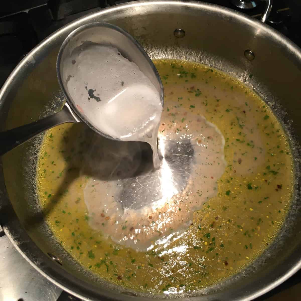 Ladle of starchy pasta cooking water added to clam sauce with heat cranked to bring to a high simmer
, emulsifying the pasta with clams.
