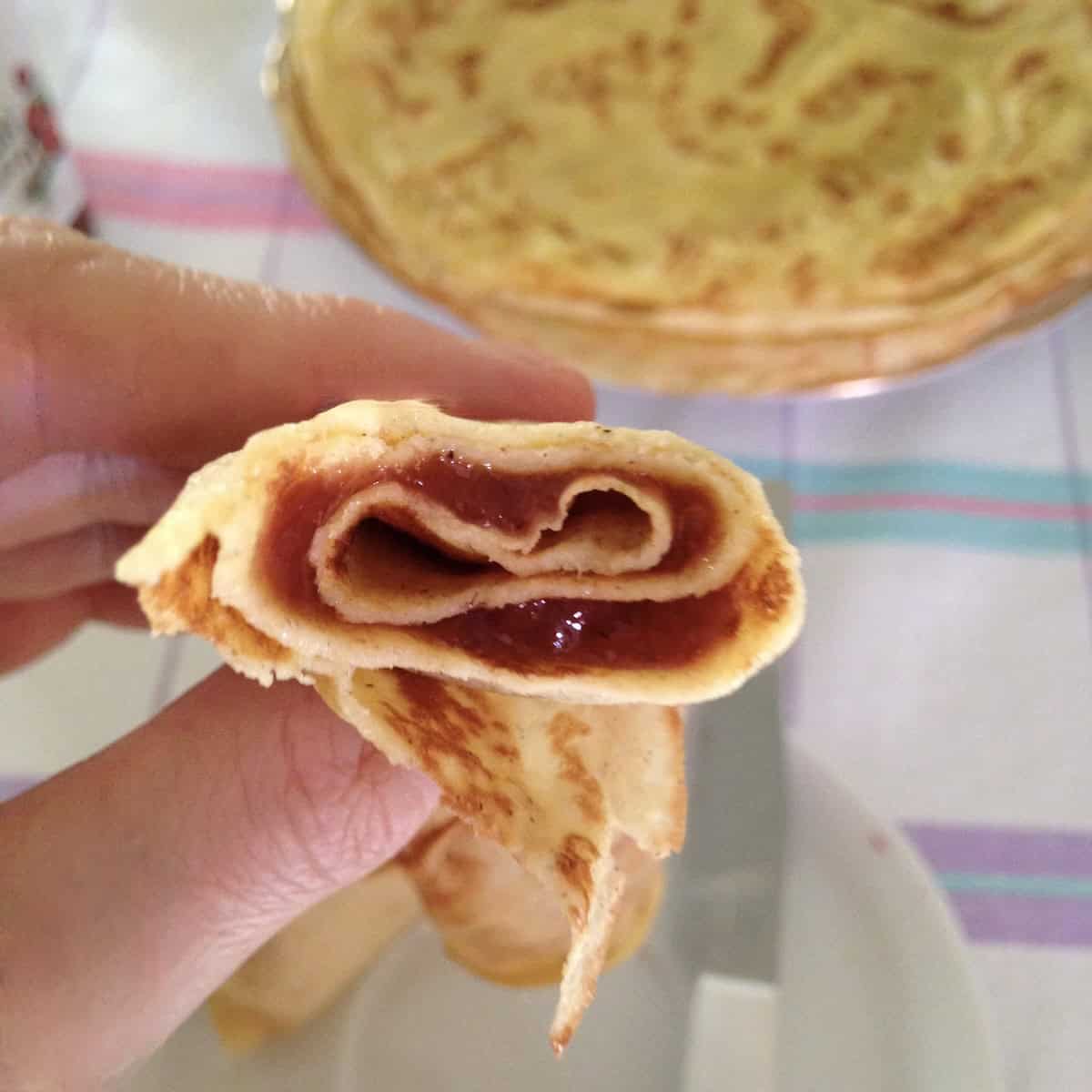 Sweet crepe filled with strawberry jam with a bite taken out, showing the thin tender texture of homemade French crepes.