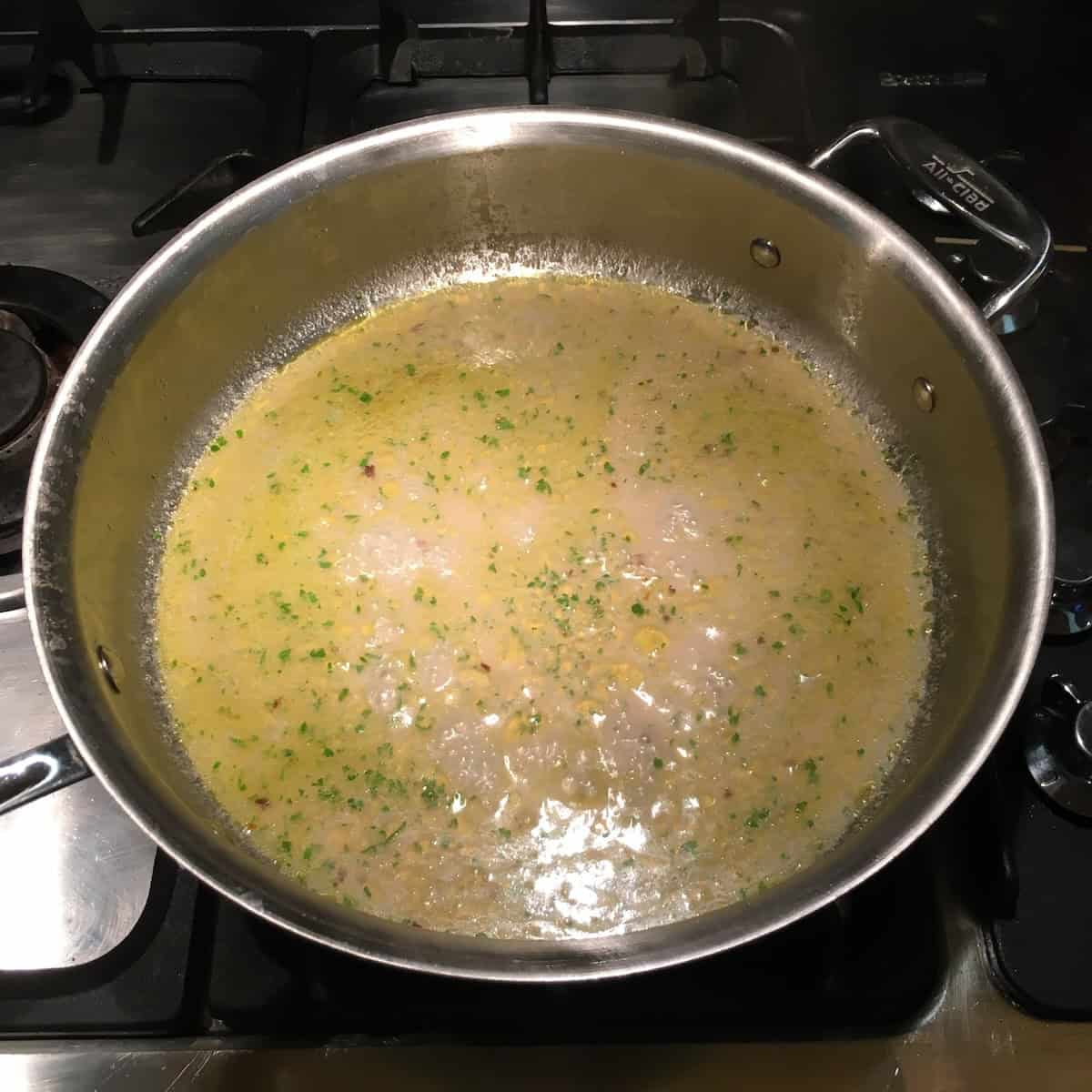 Starchy pasta water and clam sauce at a simmering boil ready to add pasta for mantecatura, emulsifying the vongole sauce.