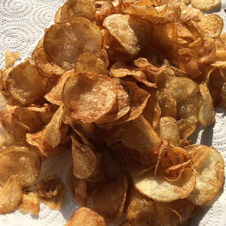 super thin and crispy homemade potato chips on a white paper towel in the sunlight