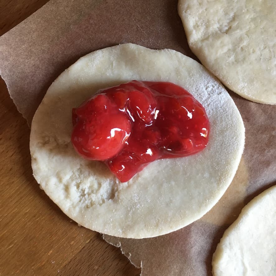 Pie filling placed onto a cutout round of dough ready to be closed and sealed.