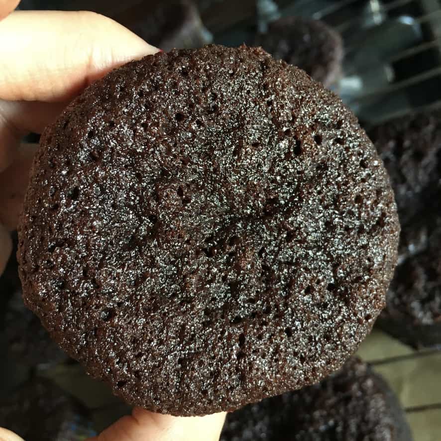 hand holding a devil's food cupcake after it's completely cooled and now the color has become even darker and you can see how moist the cupcake is